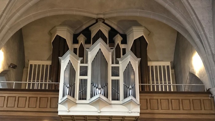 Elegante Pfeifenorgel auf einer erhöhten Plattform in einem gewölbten, historischen Kircheninnenraum.