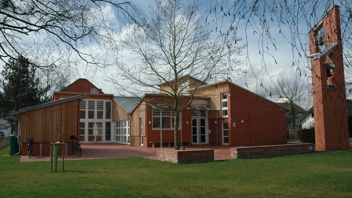 Moderner Gebäudekomplex mit Holz- und Ziegelfassaden in einer grünen Außenanlage mit Bäumen.