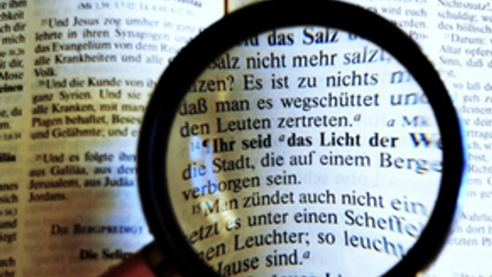 Eine Lupe hebt deutschen Text in einem aufgeschlagenen Buch hervor und fokussiert sich auf bestimmte Wörter.