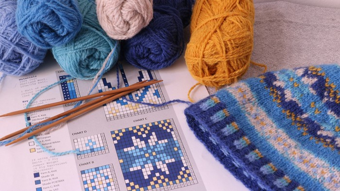 Foto af garn, strikkepinde, stikkeopskrift og en færdigstrikket blå hue