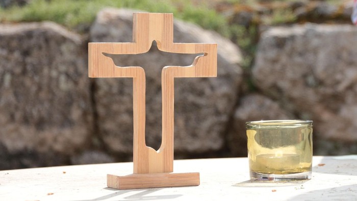 Holzkreuz mit einer Kerze in einem kleinen Glasbehälter auf einer Steinfläche im Freien.