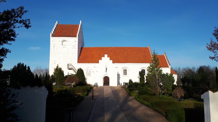 Et hvidt kirkebygning med røde tag og en smuk have foran