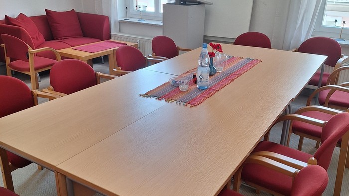 Ein moderner Besprechungsraum mit einem großen Holztisch, roten Stühlen und einer Couch.