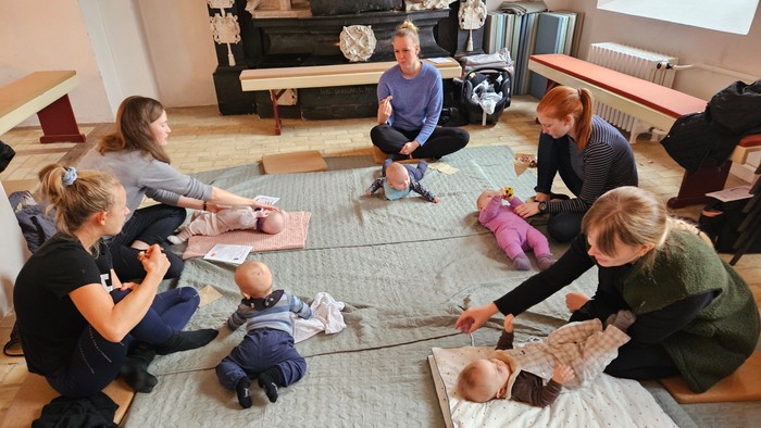 En gruppe voksne og babyer deltager sammen i en guidet gulvøvelse eller holdtime.