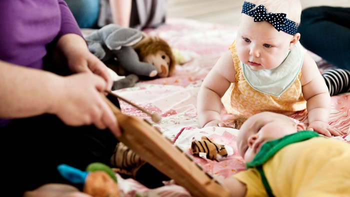 En voksen hånd holder et billede frem for to spillende børn på en gulvetæppe.