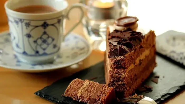 Lækkert stykke chokoladekage serveret med en kop te og kaffe på et rustikt skiferfad.