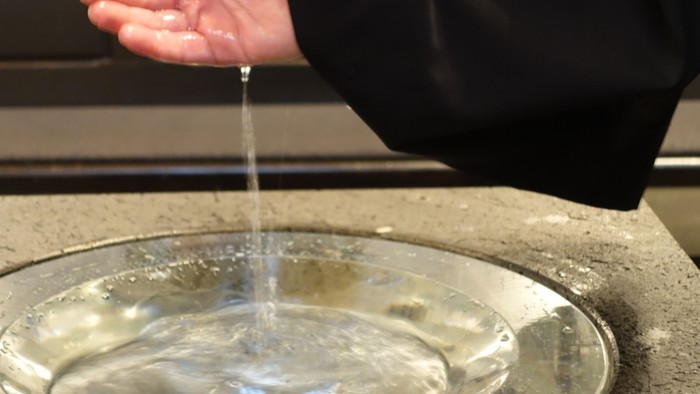 Person wäscht sich die Hände über einer Metallschale
