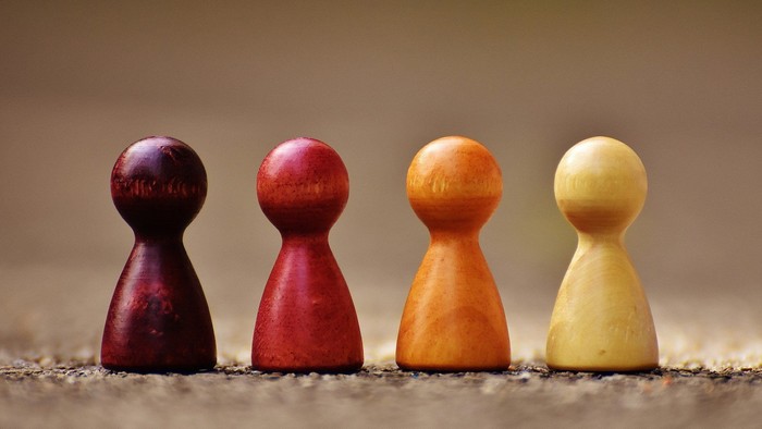 Vier bunte Holzsteckfiguren in einer Reihe auf einer strukturierten Oberfläche angeordnet.