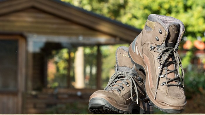Die braunen Wanderstiefel stehen vor einer Holzhütte im Wald.