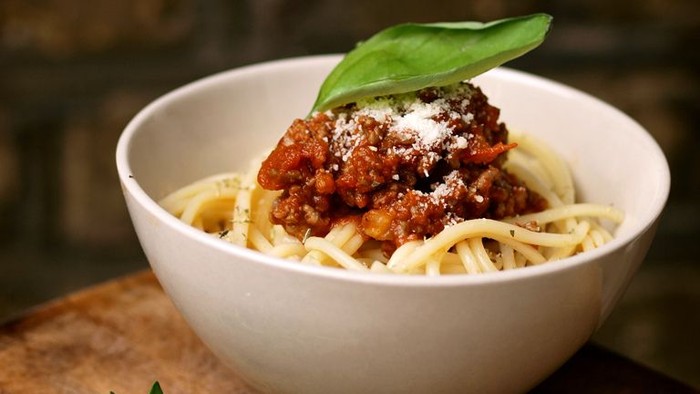 En bolle med spaghetti i tomatsoace, garnished med frisk basilika og parmesan.