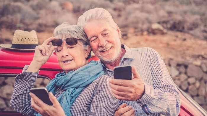 Ein älteres Paar posiert mit Handys an einem Strand.