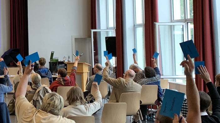 Eine Gruppe von Menschen in einem Raum hält blaue Karten hoch.