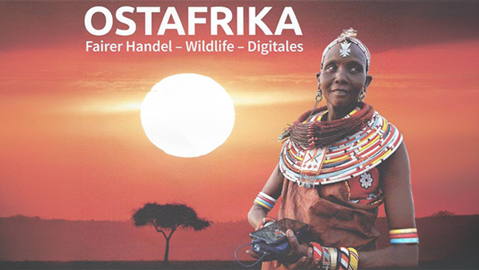Das Bild zeigt ein Plakat mit dem Titel „OSTAFRIKA“ in großen weißen Buchstaben. Darunter stehen die Begriffe „Fairer Handel – Wildlife – Digitales“. Im Vordergrund ist eine Frau in traditioneller Kleidung mit farbenfrohen Halsreifen und Schmuck zu sehen