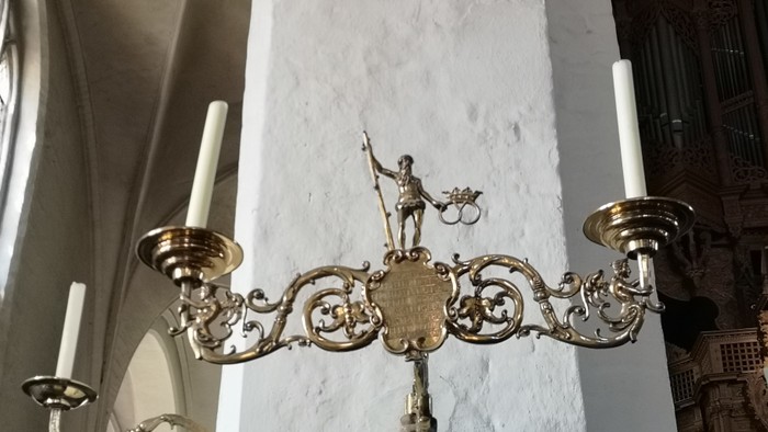 Verzierter Kronleuchter mit Kerzenhaltern und einer dekorativen Statue in einem historischen Innenraum.