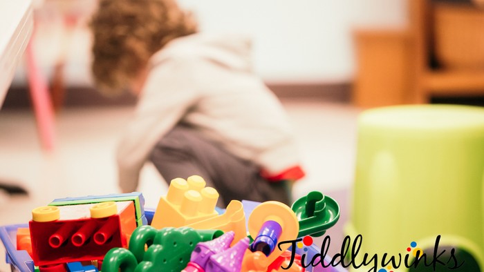 A child plays with colorful toys on the floor, with a tray of toys in the foreground.