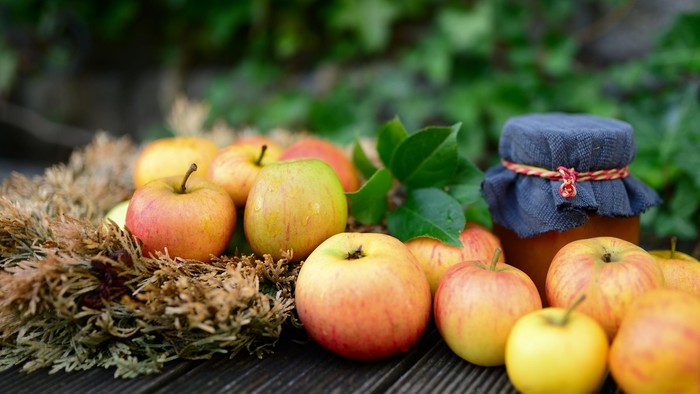 En samling æbler og en glass med marmelade på en trædeks.