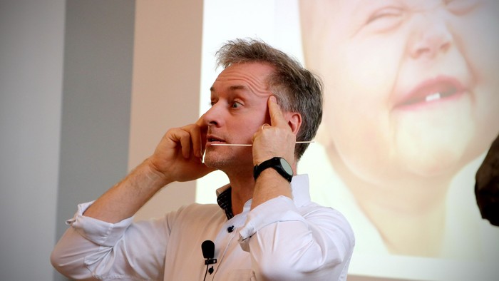 Mand, der taler i en telefon, mens et projiceret billede af en persons ansigt vises bag ham.