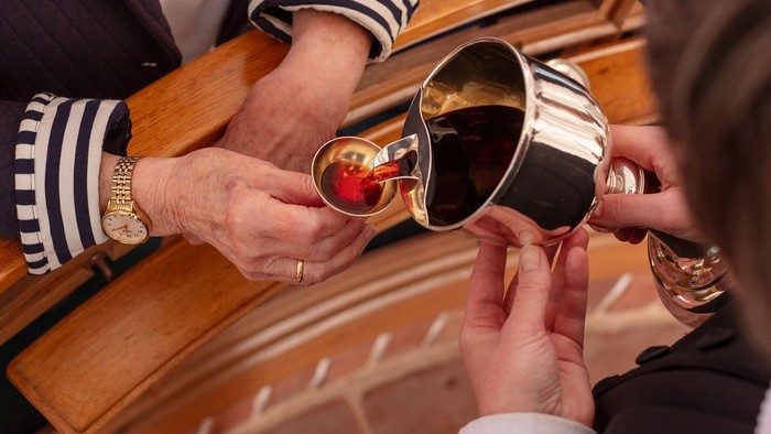 Hænder, der deltager i en vin-deleritual under en religiøs ceremoni, hvor der bruges en fælles kop.