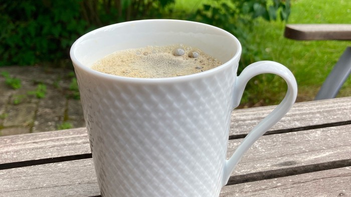 En hvid tepibeholder med kaffekaffe på træbæn i have