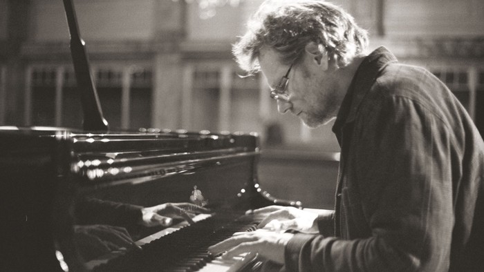 En fokuseret pianist dybt optaget af at spille på et opretstående klaver i en rolig omgivelse.