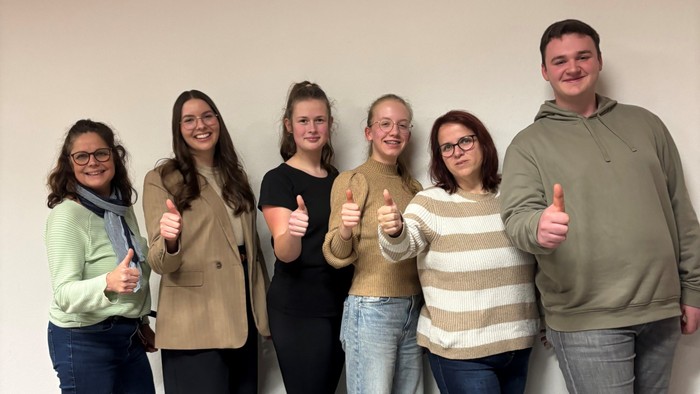 Eine Gruppe von sechs Personen, die lässig gekleidet gemeinsam mit Daumen hoch posieren.