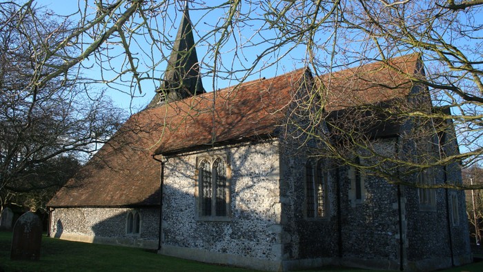Small stone church with steep thatched roof and tall spire, surrounded by trees.