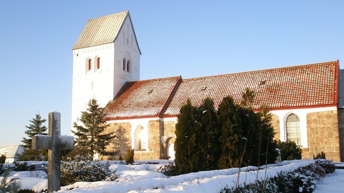 En snedækket kirke med tårn og røde tagfliser.