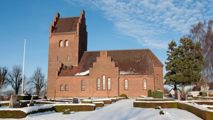 En rød murstenskirke med tårn og tagtag i sneklædt landskab