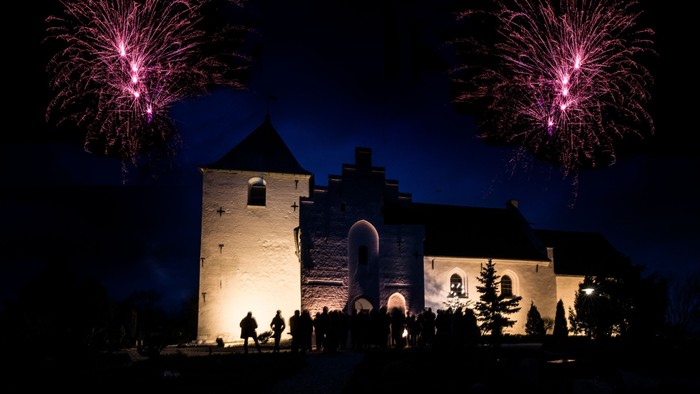 En middelalderlig kirke belyset ved natten med fyrværkeri i himlen
