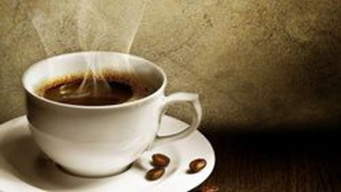 En kop kaffe med damp, der stiger op, placeret på en underkop med nogle kaffebønner ved siden af.