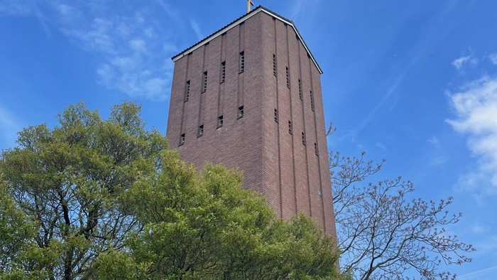 Turm mit Kreuz auf dem Dach, umgeben von Bäumen unter blauem Himmel