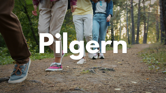 Gruppe von Menschen, die gemeinsam auf einem Waldweg wandern, mit dem überlagerten Wort „Pilgern“.