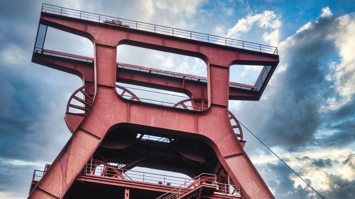 Das Bild zeigt einen Bergbau-Förderturm vor einem blauen Himmel mit Wolken.