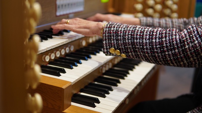 Hands playing an organ with black and white keys.