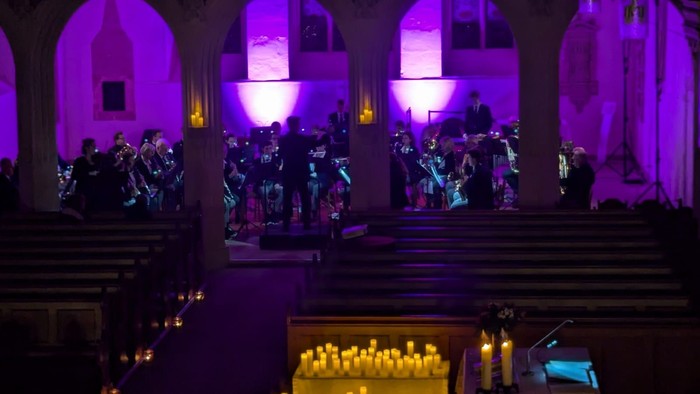 Orchester, das in einer prächtigen, violett beleuchteten Kathedrale mit Reihen angezündeter Kerzen im Vordergrund spielt.