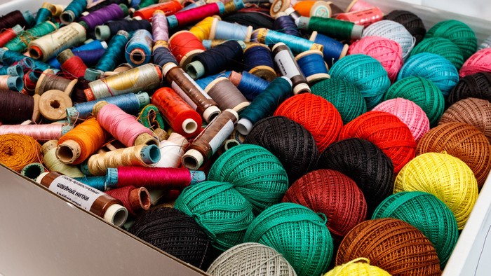 Bunte Garnspulen und Knäuel dicht gepackt in einem Behälter.