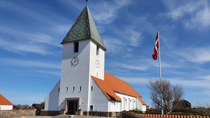 En hvid kirke med klokketårn og en rød tag, med en dansk flag på en stang ved siden af.