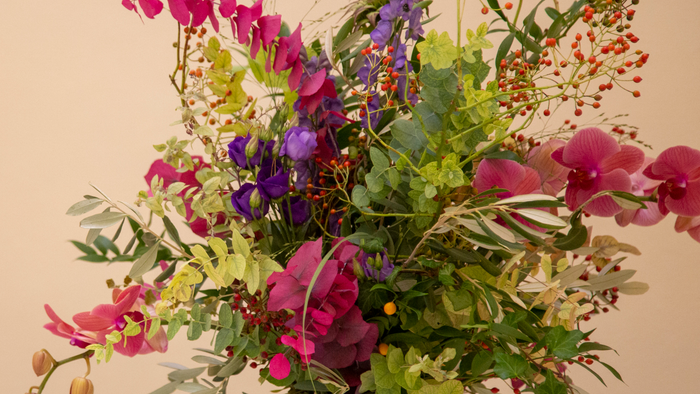 Livligt buket med lyserøde, lilla blomster, grønt løv og røde bær i en frodig sammensætning.