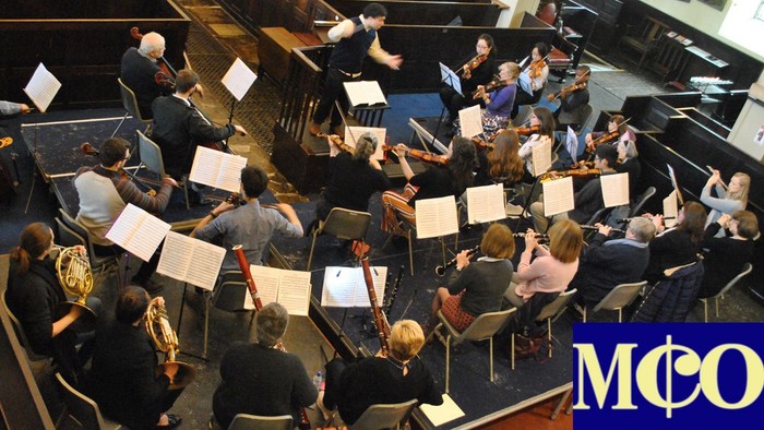 Orchestra rehearsing with sheet music stands.