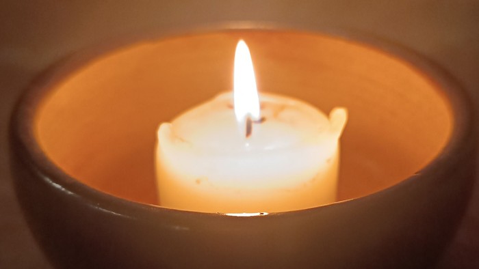 Eine brennende Kerze in einer dunklen, warmtönigen Schale, die sanftes, mildes Licht wirft.