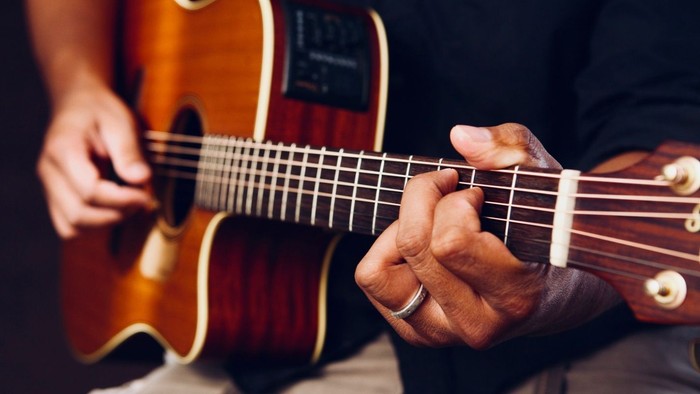 En person, der spiller på en akustisk guitar med præcis håndplacering på strengene.