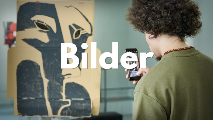 Eine Person macht ein Foto von einem abstrakten Kunstwerk in einer Galerie, wobei das Wort „Bilder“ eingeblendet ist.