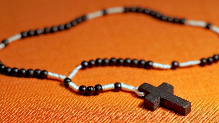 Ein schwarzes Kreuz hängt an einer Perlenkette auf einem orangen Hintergrund