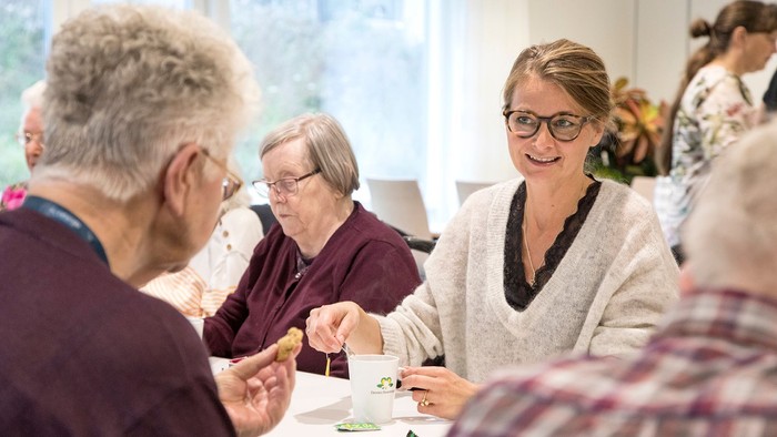 En gruppe mennesker, der nyder et måltid og samtale sammen i en hyggelig indendørs atmosfære.