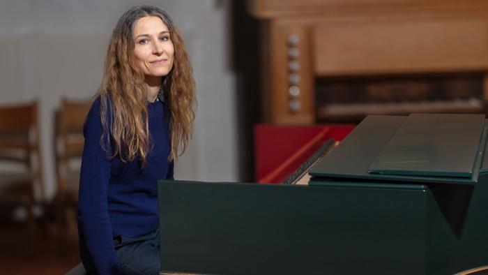 En kvinde sitter ved et grønt piano og ser op.