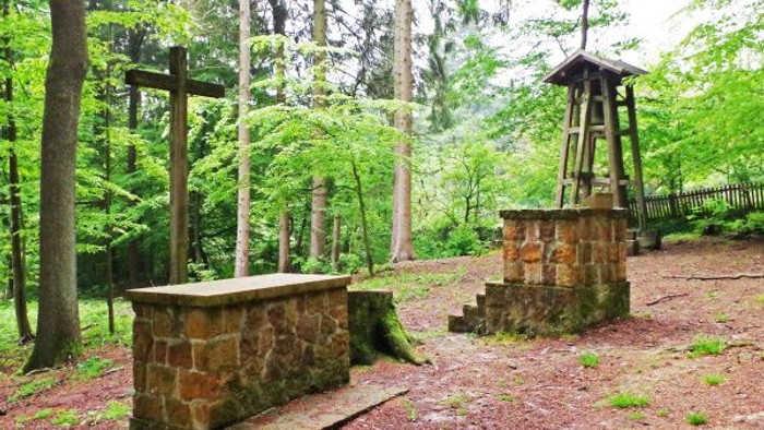 Ein friedvoller Waldschrein mit Steinbänken, Kreuzen und einem kleinen hölzernen Aussichtsturm.