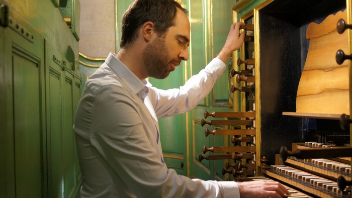 En mand spiller på et indviklet designet orgel i et rum med grønne paneler.