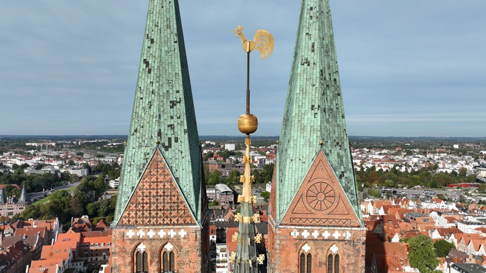 Zwei grüne Kirchturmspitzen mit goldenen Wetterfahnen über einem roten Dachgebiet