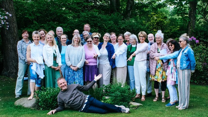 En glad gruppe poser udendørs i en have, hvor en mand leger med at ligge på græsset.