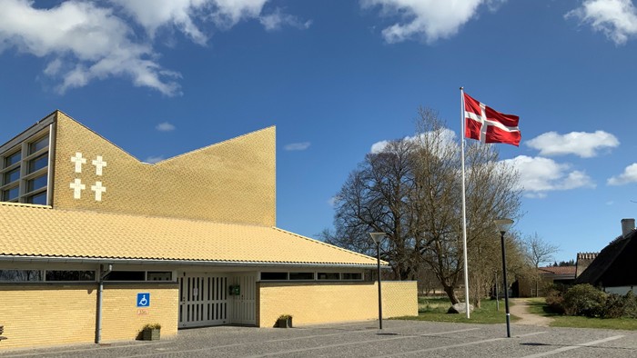 Gul kirke med kors og dansk flag på en klar dag